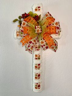 a cross made out of fabric with flowers and leaves on it's side, hanging from the wall