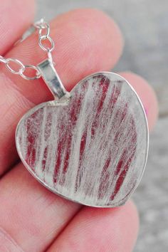 a hand holding a heart shaped pendant with red and white frosting on the inside