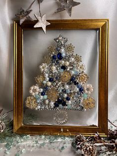 a christmas tree made out of beads and other items in a gold frame on a table