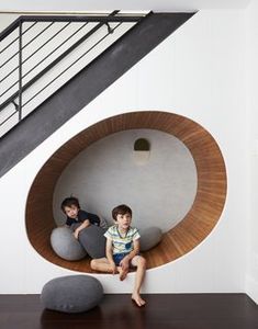 two young boys sitting in a circular chair on top of a wooden floor next to a stair case