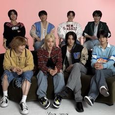 the group of young men are sitting on a couch together in front of a pink wall