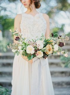 a bride holding a bouquet of flowers in her hands and standing on some steps outside