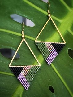 a pair of triangle shaped earrings sitting on top of a green leaf