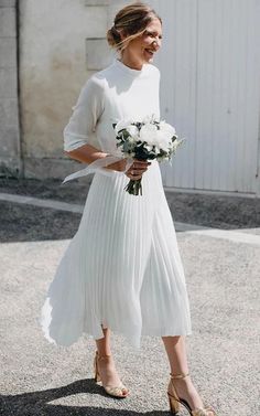 a woman in white is walking down the street with her bouquet and smiling at someone