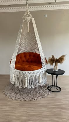 a white hammock chair with an orange cushion on it and a side table