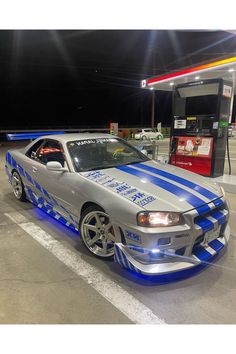 a silver car with blue stripes parked in front of a gas station at night time