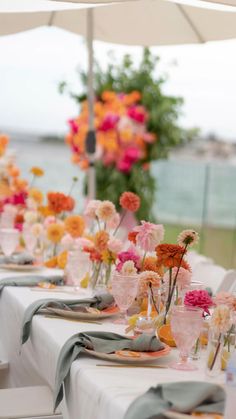 the table is set with many different colored flowers in vases and glassware on it