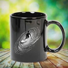 a black coffee mug with a man surfing on a wave in the middle of it