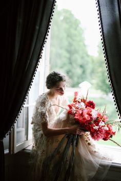 a woman sitting on a window sill holding a bouquet of flowers