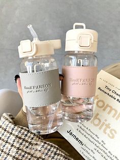 two water bottles sitting next to each other on top of a table with an open book