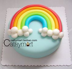 a rainbow shaped cake with white clouds and blue frosting on top, sitting on a plate