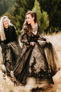 two women in long black dresses walking through tall grass