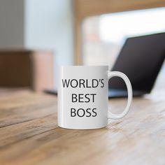 a white coffee mug that says world's best boss on it sitting in front of a laptop