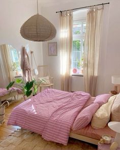 a bedroom with pink and white bedding, windows, curtains and plants in the corner