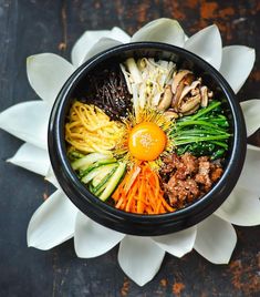 a bowl filled with noodles, meat and veggies on top of a white flower