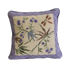 an embroidered pillow with purple trim and flowers on the front, sitting on a white surface