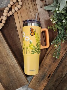 a yellow travel mug with a butterfly painted on it and flowers in the foreground