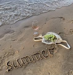 the word summer written in sand next to a bowl of grapes and a glass of wine