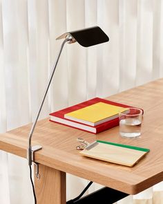 a desk with a lamp, books and a glass on the table next to it