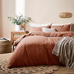 a bed with an orange comforter in a bedroom next to a basket and potted plant