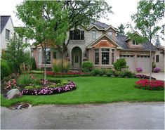 a house with landscaping in front of it and flowers around the yard on the lawn