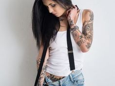 a woman with tattoos on her arms and shoulder holding a black bag in front of her face