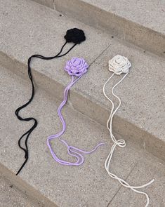 three crocheted flowers sitting on the steps next to each other, one purple and one black