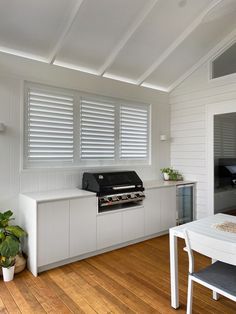 a kitchen with white walls and wooden flooring next to a dining room table that has a grill on it