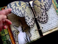 a hand holding an open book with two butterflies on it and another butterfly in the middle