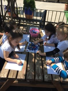 four children sitting at a picnic table with paper and pencils in their hands as they draw