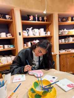 a woman sitting at a table with some art supplies