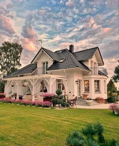 a large white house sitting in the middle of a lush green field with pink flowers