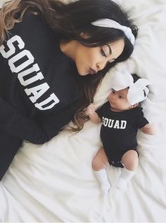 a woman laying on top of a bed next to a baby wearing a shirt that says squad