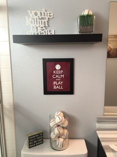 a bathroom with a toilet and some shelves above it that says keep calm play ball