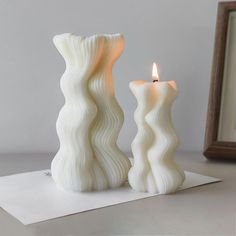 two white candles sitting on top of a piece of paper next to a framed photo