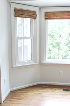 an empty room with wood floors and two windows that have blinds on them in the corner