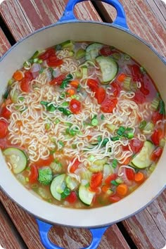 a pot filled with noodles and vegetables on top of a wooden table