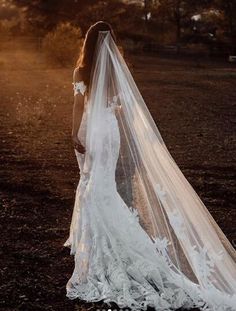 a woman in a wedding dress with a veil on her head standing in the middle of a field