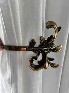 a gold colored metal curtain tie on top of a white drapes with an ornate design