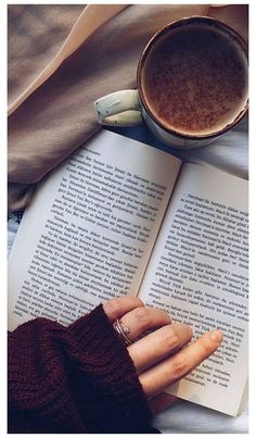 a person laying on top of a bed reading a book next to a cup of coffee