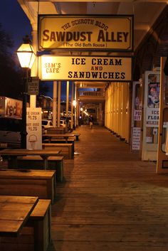 the sidewalk is lined with wooden benches and signs for ice cream and sandwiches on it