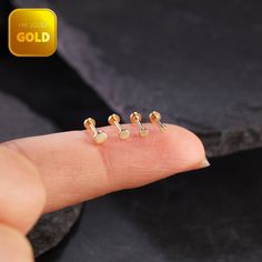 three tiny gold ear studs on someone's finger