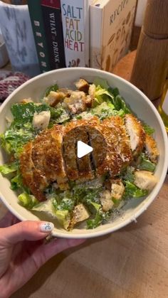 a person holding a bowl of food with meat on it and salad in front of them