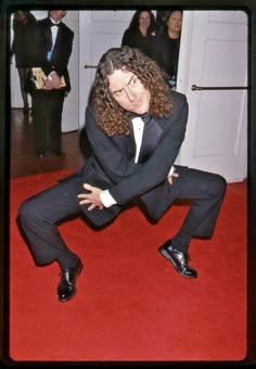 a man in a tuxedo poses on a red carpet with his arms crossed