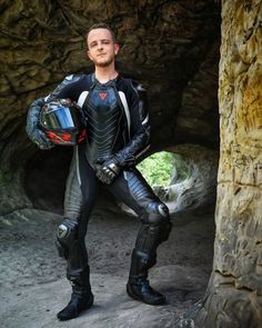 a man in a black and white suit holding a helmet standing next to a rock formation