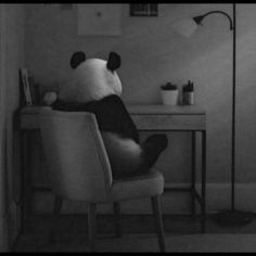 a black and white photo of a panda bear sitting on a chair in front of a desk