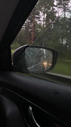 the side view mirror of a car with rain on it's glass and trees in the background