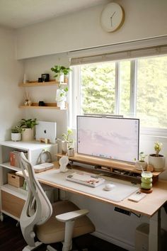 a desk with a computer on it in front of a window and some shelves filled with plants