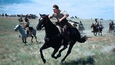 a man riding on the back of a black horse next to other horses in a field