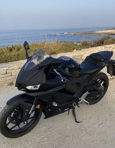 a black motorcycle parked on the side of a road next to the ocean and rocks